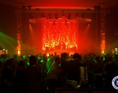Konzertbühne mit rot-orangefarbener Beleuchtung und Publikum in grünem Laserlicht bei Indoor-Veranstaltung