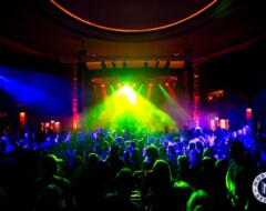 Konzertbühne mit bunter Lichtshow in Grün, Gelb und Blau vor tanzendem Publikum in einem Club