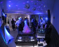Hochzeits-DJ-Pult mit Controller und Laptop vor tanzenden Hochzeitsgästen in blau beleuchtetem Saal mit Discokugeln