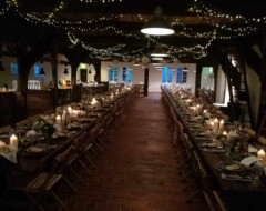 Festlich dekorierter Hochzeitssaal mit langen Tafeln, Lichterketten, Kerzen und holzfarbenen Stühlen