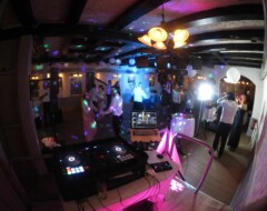 DJ-Equipment im Vordergrund einer Hochzeitsfeier mit tanzenden Gästen unter bunter Beleuchtung in Eventlocation