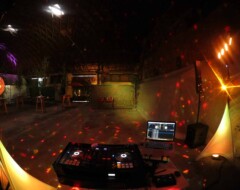 DJ-Equipment mit beleuchteten Reglern und Laptop vor nächtlicher Outdoor-Location mit rotem Lichteffekt