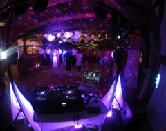 DJ-Pult mit Laptop und Mischpult im Vordergrund, dahinter tanzende Hochzeitsgäste unter bunter Partybeleuchtung und Lampions