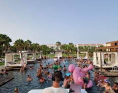 DJ legt Musik bei einer Pool-Party auf, während zahlreiche Gäste im Wasser feiern und auf Luftmatratzen treiben