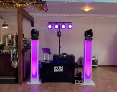 DJ-Setup mit lila beleuchteten Säulen, Scheinwerfern und Mischpult von Sven Baker in festlich geschmücktem Veranstaltungsraum