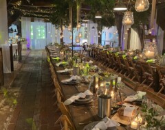 Festlich gedeckte Hochzeitstafel mit rustikalen Holztischen, Lichterketten und hängenden Kerzen in einer Scheune