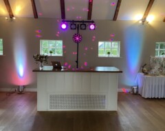 DJ-Pult mit Lichtanlage und bunten Lichteffekten in rustikaler Hochzeitslocation mit Holzbalkendecke und Lichterkette