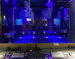 DJ-Pult mit Pioneer-Equipment vor blau beleuchteter Tanzfläche und Bühne mit Ballondekoration in einem Club